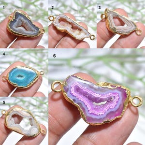 Könnte beinhalten: Auswahl an Edelsteinanhängern mit goldfarbenen Rändern. Die Anhänger zeigen verschiedene Farben, darunter Blau, Lila und Weiß, mit einzigartigen inneren Kristallformationen. Jeder Anhänger hat zwei Schlaufen zum Befestigen an Schmuck.