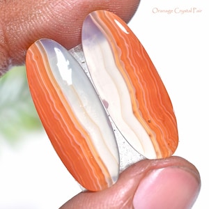Könnte beinhalten: Zwei ovale, orange und weiße Achatsteine. Die Steine haben ein gestreiftes Muster mit orangefarbenen und weißen Bändern. Der Text "Oranage Crystal Pair" ist in der oberen rechten Ecke sichtbar.