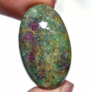 May include: An oval-shaped gemstone with a mix of green, red, and brown hues. The stone has a polished surface, with visible inclusions and variations in color. The overall appearance is natural and earthy, with a blend of textures.