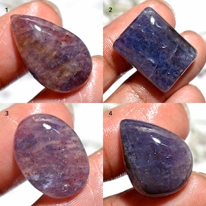 Puede incluir: Cuatro piedras preciosas pulidas de varias formas. Las piedras muestran tonos de púrpura, azul y marrón. Cada piedra tiene una superficie lisa y brillante, con patrones e inclusiones internas visibles. Las piedras preciosas son sostenidas por una persona.