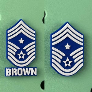 May include: Two blue and white military rank insignia, one with the name "BROWN" at the bottom. The insignia features a star and stripes design. The background is a light green color.