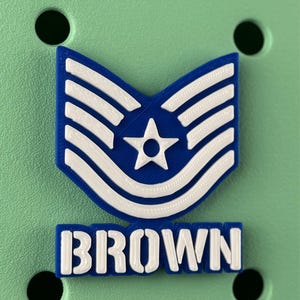 May include: A blue and white military insignia with a star and stripes design, and the name "BROWN" in white block letters. The insignia is set against a light green background.