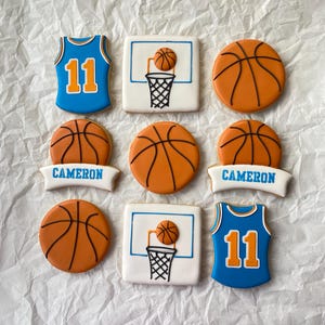 May include: Nine decorated sugar cookies with basketball themes.  The cookies feature basketballs, basketball jerseys, and basketball hoops.  One cookie has the name "CAMERON" on it.  One cookie has the number "11" on it.