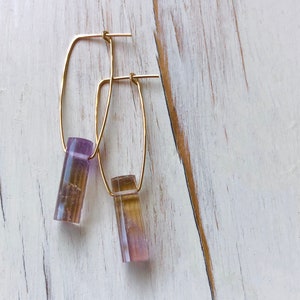 May include: A pair of gold hoop earrings with a purple and brown crystal pendant hanging from each hoop.
