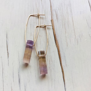 May include: A pair of gold hoop earrings with a purple and brown rectangular stone hanging from each hoop.