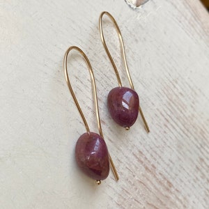 May include: A pair of gold earrings with a teardrop-shaped, deep red gemstone.