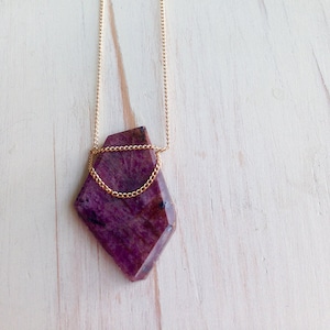 May include: A gold chain necklace with a large, faceted, purple gemstone pendant.