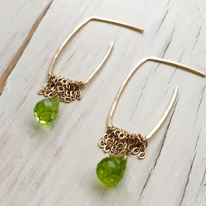 May include: Gold earrings with a teardrop shaped green peridot stone and a dangling chain of gold beads.