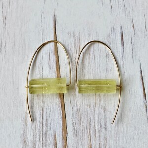 May include: A pair of gold hoop earrings with a light green stone bar in the center of each hoop.