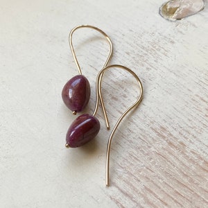 May include: A pair of gold earrings with a teardrop-shaped purple gemstone hanging from each.
