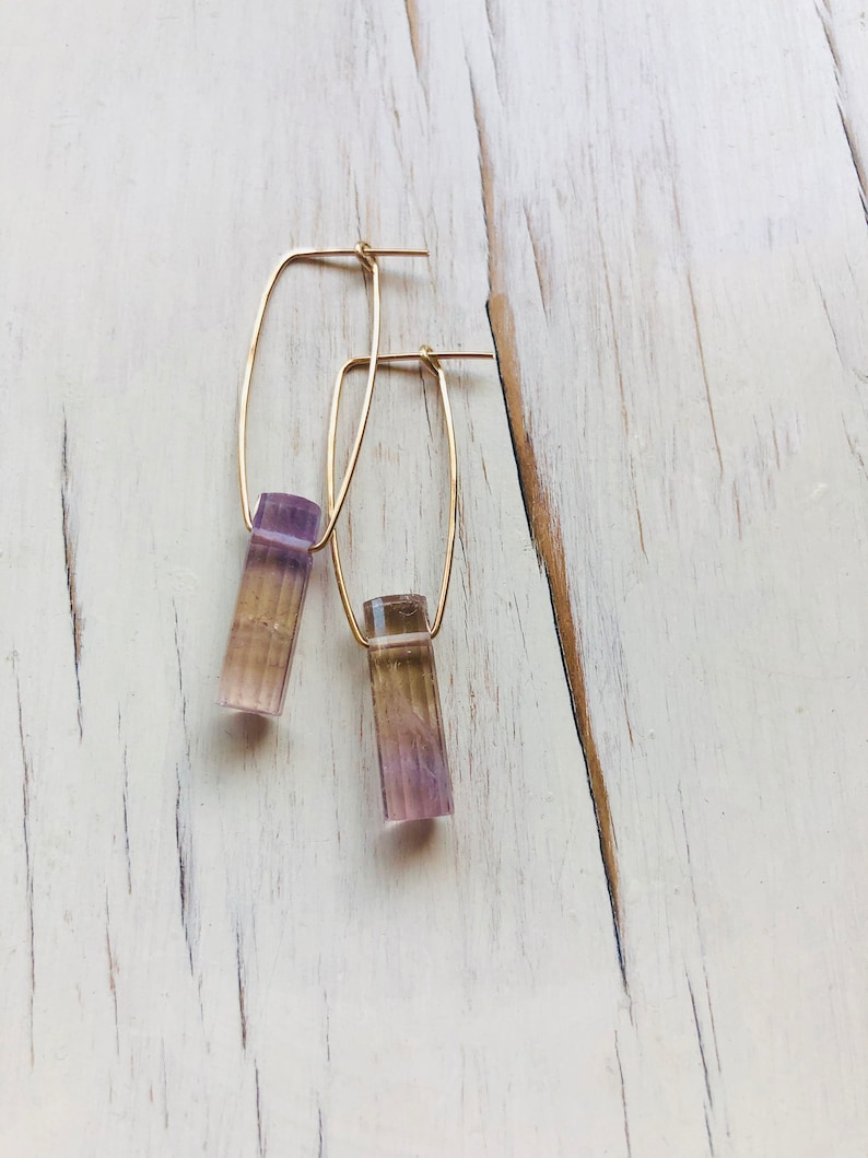 May include: A pair of gold hoop earrings with a purple and brown rectangular stone hanging from each hoop.