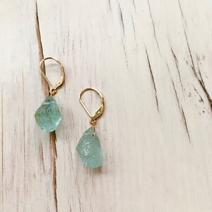 Peut inclure: Une paire de boucles d'oreilles en or avec des pierres d'aigue-marine bleu clair. Les pierres sont brutes et ont une forme naturelle irr&eacute;guli&egrave;re.