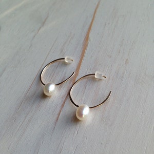 May include: A pair of gold hoop earrings with a single white pearl dangling from each hoop.