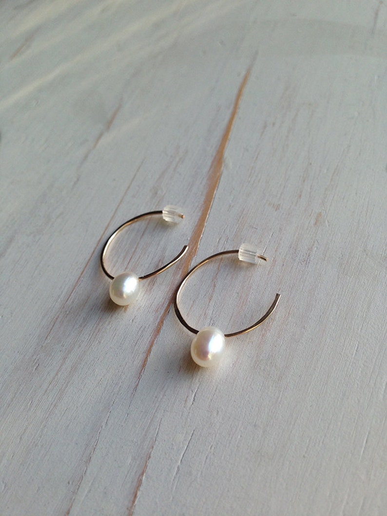 May include: A pair of gold hoop earrings with a single white pearl dangling from each hoop.