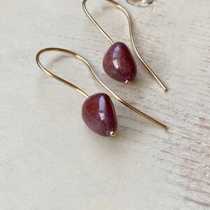 May include: A pair of gold earrings with teardrop-shaped purple stones.
