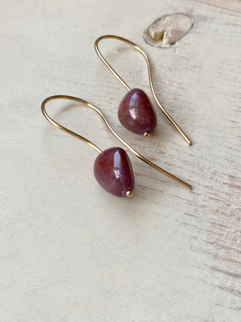 May include: A pair of gold earrings with teardrop-shaped purple stones.