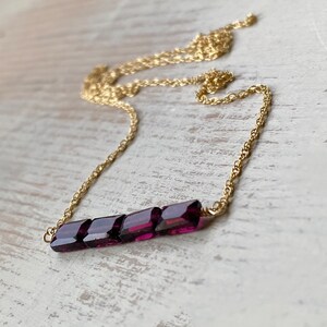 May include: A gold chain necklace with a bar pendant made of multiple faceted purple gemstones.