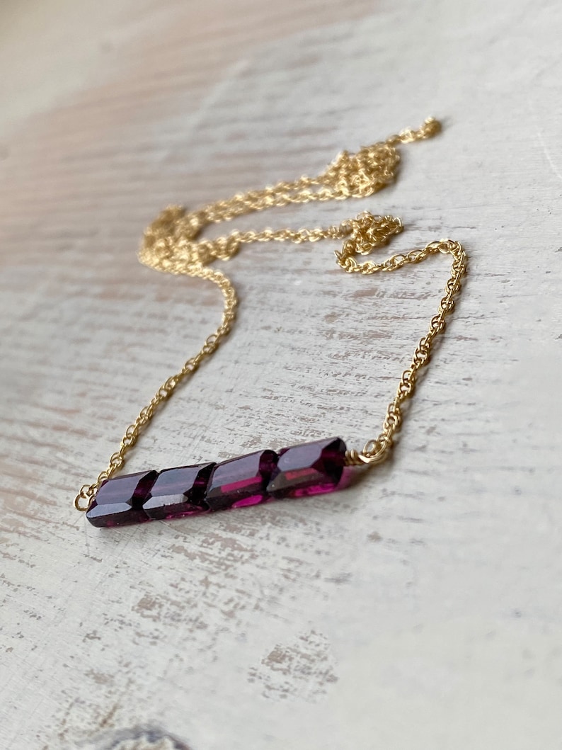 May include: A gold chain necklace with a bar pendant made of multiple faceted purple gemstones.
