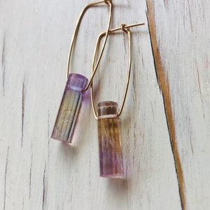 May include: A pair of gold hoop earrings with a purple and yellow crystal pendant on each hoop.