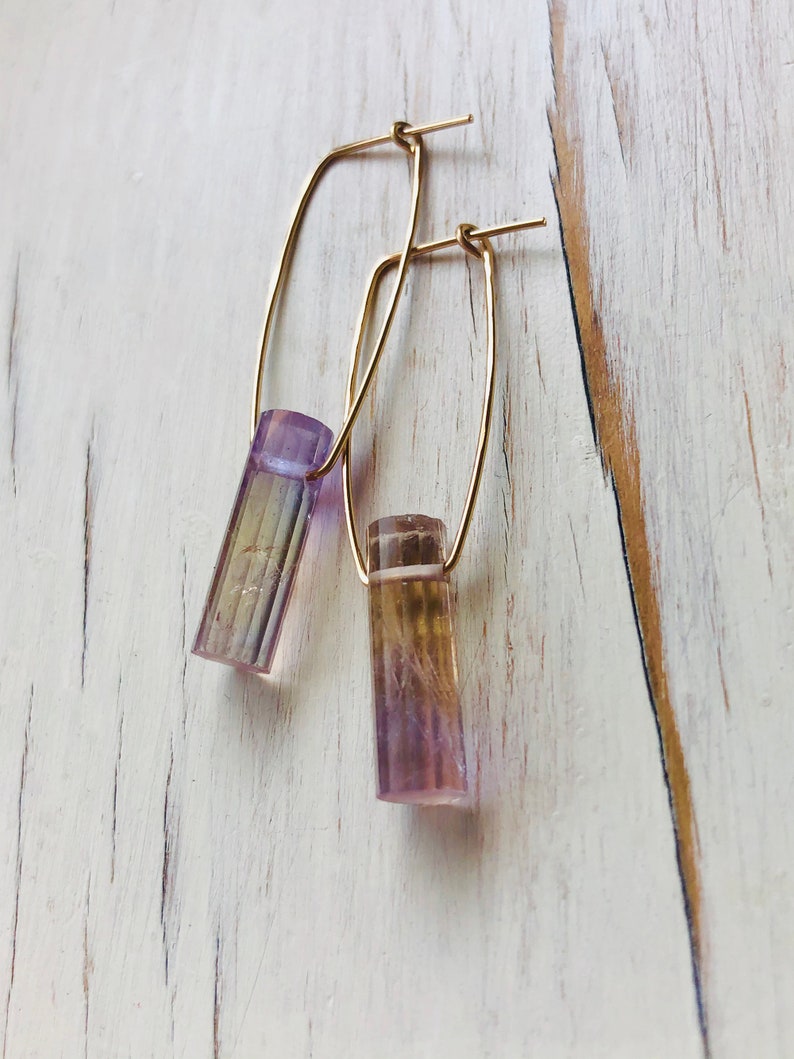 May include: A pair of gold hoop earrings with a purple and yellow crystal pendant on each hoop.