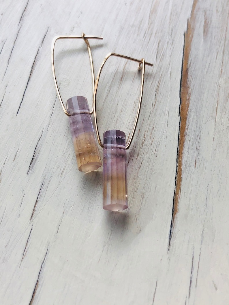May include: A pair of gold hoop earrings with a purple and yellow crystal pendant on each hoop.