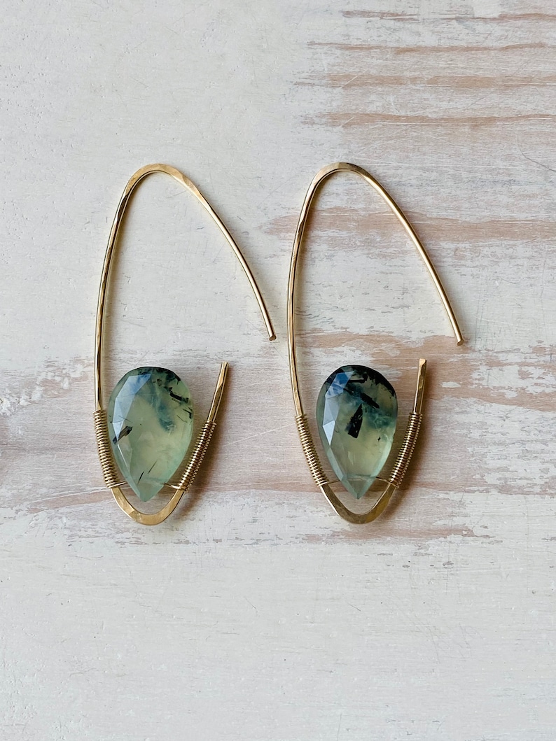 May include: A pair of gold earrings with green and black gemstone drops. The earrings are made with a simple wire design.