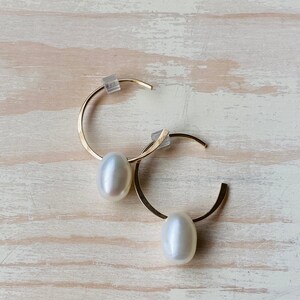 May include: A pair of gold hoop earrings with a white pearl dangling from each hoop.