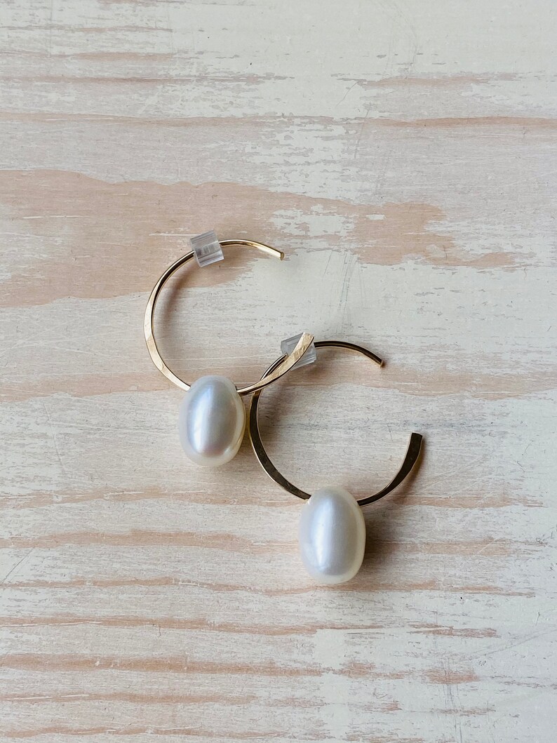May include: A pair of gold hoop earrings with a white pearl dangling from each hoop.
