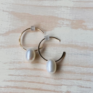 May include: A pair of gold hoop earrings with a white pearl dangling from each hoop.