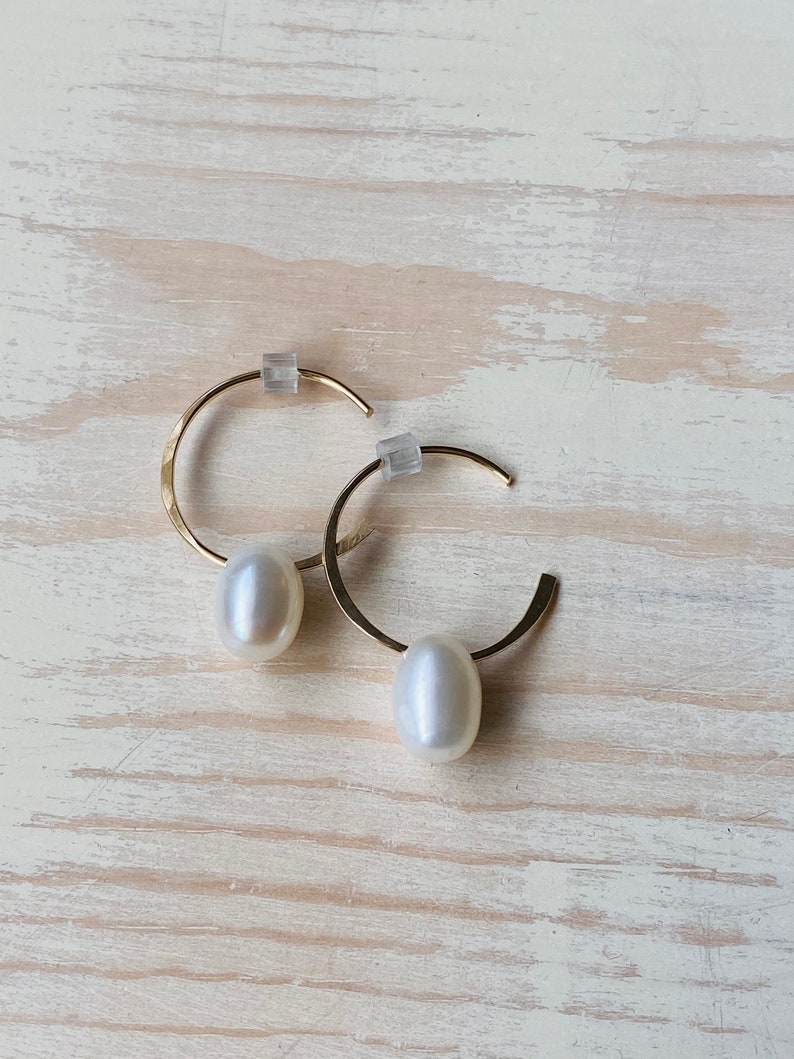 May include: A pair of gold hoop earrings with a white pearl dangling from each hoop.