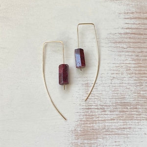 May include: A pair of gold earrings with a dark red gemstone pendant on each earring.