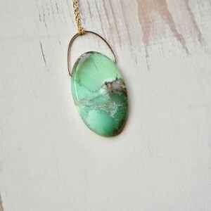 Puede incluir: Un collar de cadena dorada con un colgante ovalado de color verde y marr&oacute;n. El colgante est&aacute; hecho de una piedra natural con un patr&oacute;n &uacute;nico.