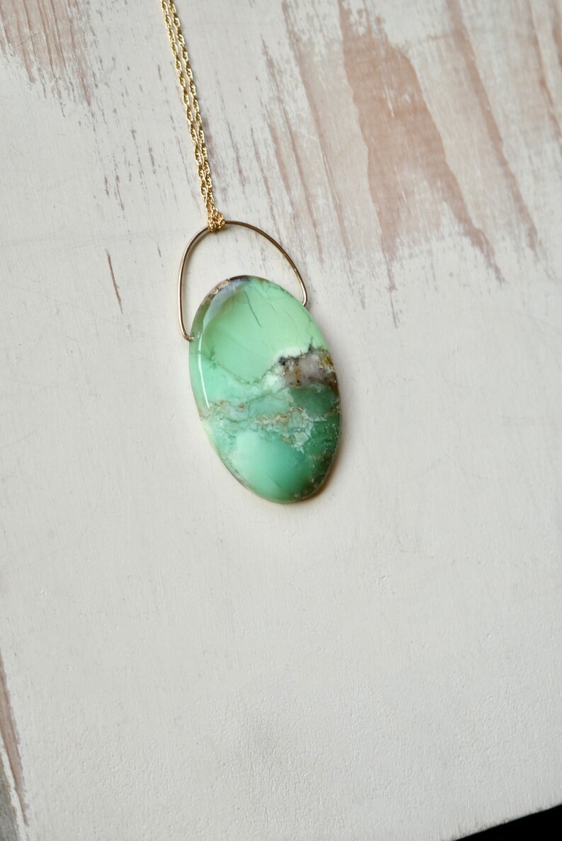 Puede incluir: Un collar de cadena dorada con un colgante ovalado de color verde y marr&oacute;n. El colgante est&aacute; hecho de una piedra natural con un patr&oacute;n &uacute;nico.