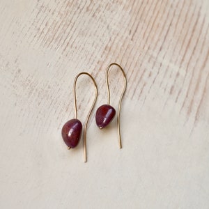 May include: A pair of gold dangle earrings with a deep burgundy gemstone on each earring.