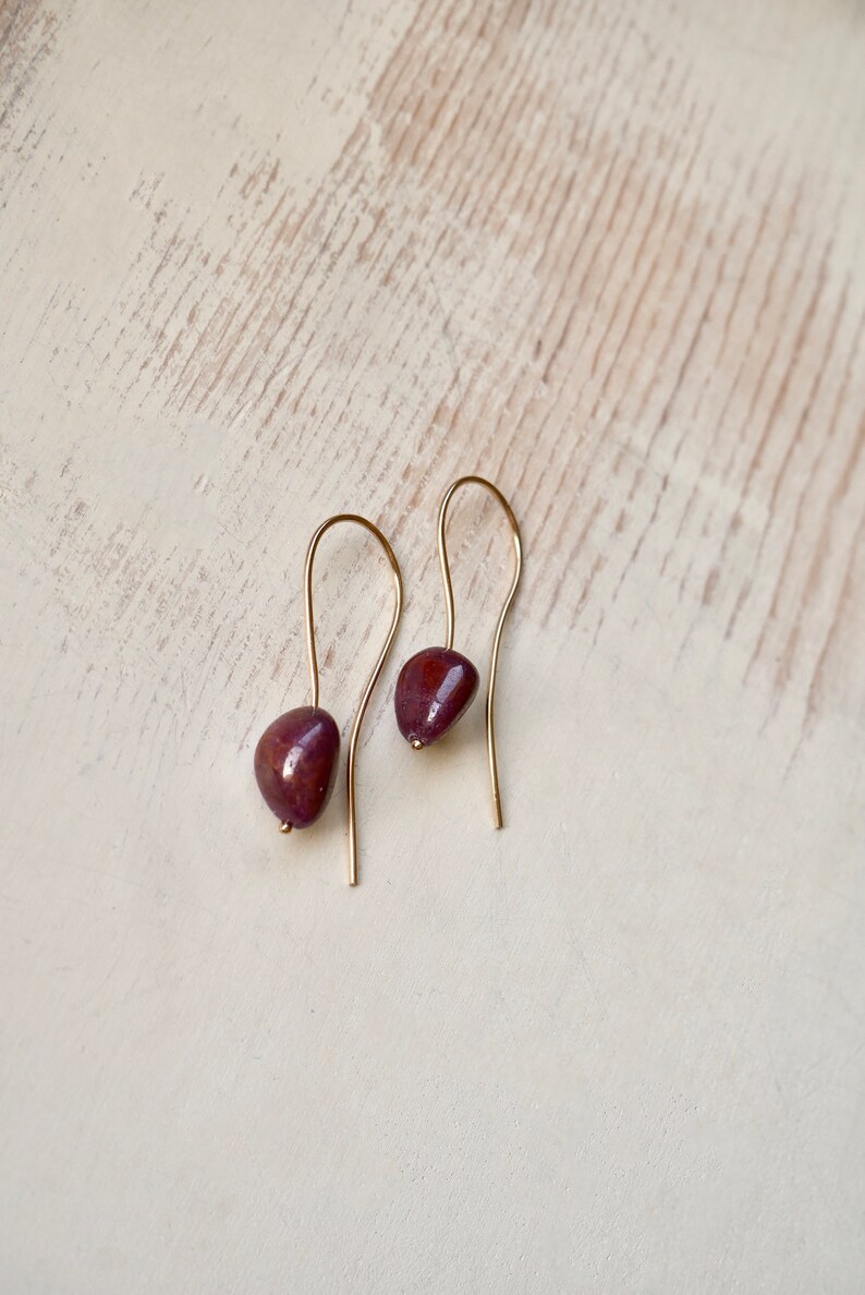 May include: A pair of gold dangle earrings with a deep burgundy gemstone on each earring.
