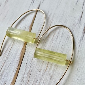 May include: A pair of gold hoop earrings with a light yellow rectangular stone hanging from each hoop.