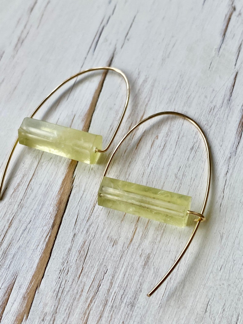 May include: A pair of gold hoop earrings with a light yellow rectangular stone hanging from each hoop.