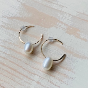 May include: A pair of gold hoop earrings with a single white pearl dangling from each hoop.