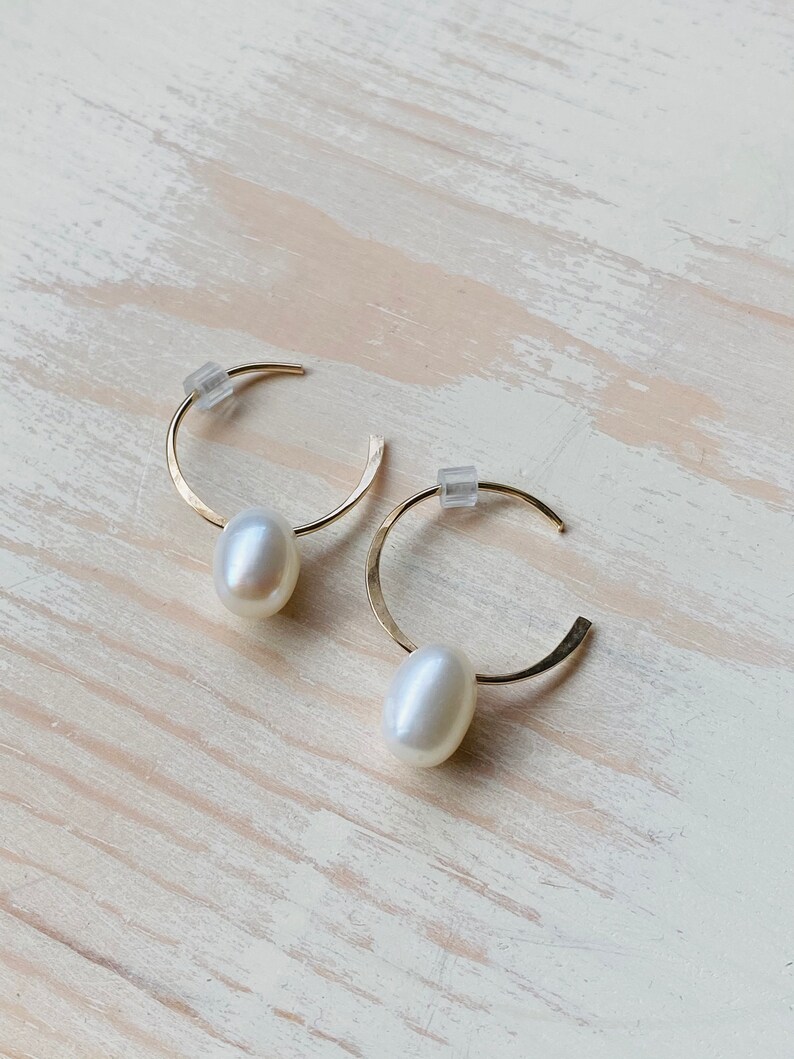 May include: A pair of gold hoop earrings with a single white pearl dangling from each hoop.