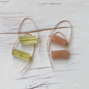 May include: A pair of gold hoop earrings with a light green and a light pink rectangular stone hanging from each hoop.