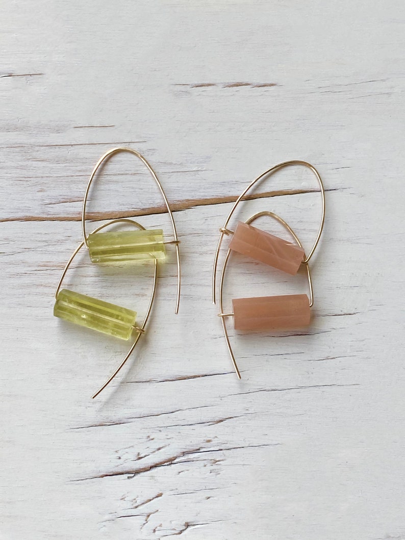 May include: A pair of gold hoop earrings with a light green and a light pink rectangular stone hanging from each hoop.