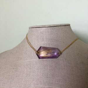 May include: A gold chain necklace with a large, faceted, purple and gold gemstone pendant.