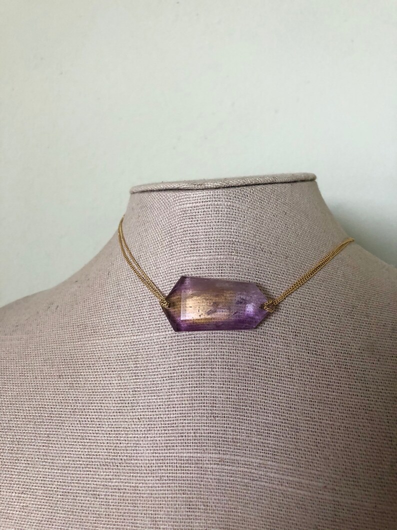 May include: A gold chain necklace with a large, faceted, purple and gold gemstone pendant.