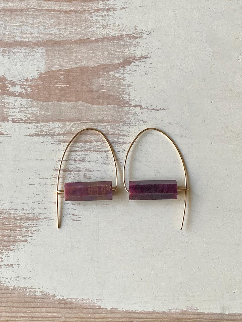 May include: A pair of gold hoop earrings with a rectangular purple stone accent. The earrings are simple and elegant.