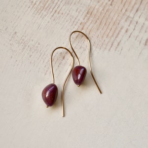May include: A pair of gold dangle earrings with a dark purple stone on each earring.