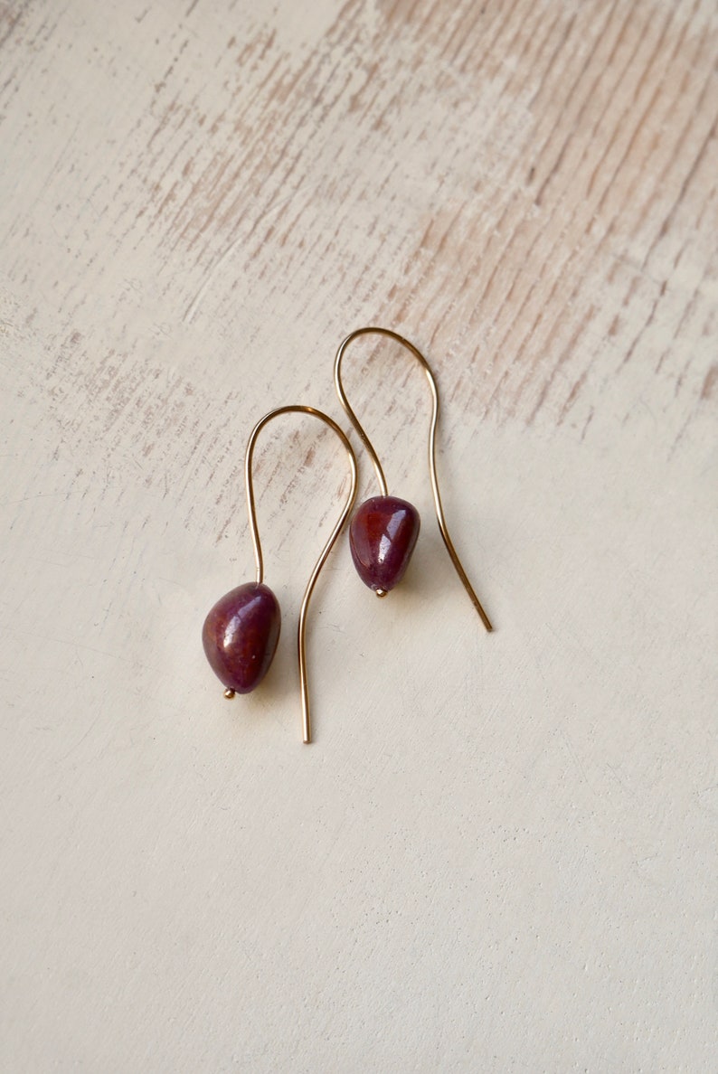 May include: A pair of gold dangle earrings with a dark purple stone on each earring.