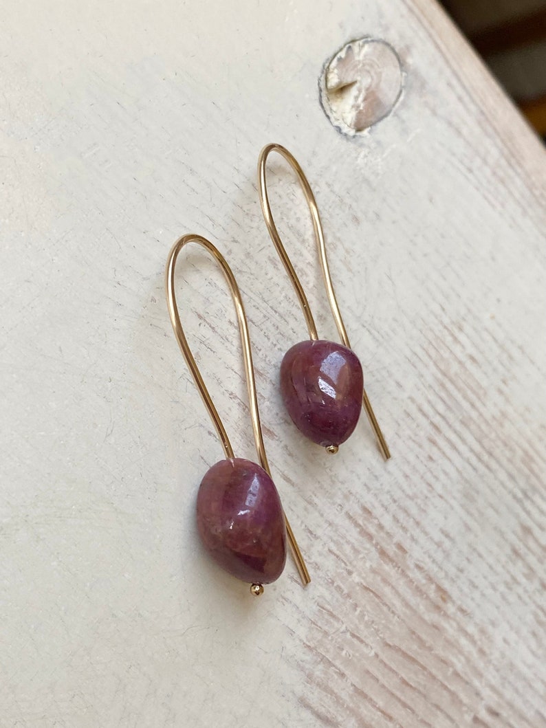 May include: A pair of gold earrings with a teardrop-shaped, deep red gemstone.
