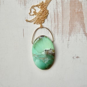 Puede incluir: Un collar con un colgante ovalado verde y marr&oacute;n con una cadena de oro. El colgante est&aacute; hecho de una piedra natural con un patr&oacute;n &uacute;nico.
