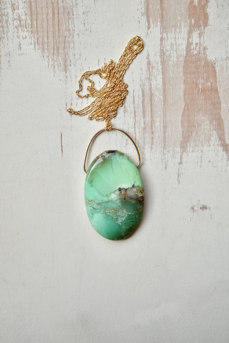 Puede incluir: Un collar con un colgante ovalado verde y marr&oacute;n con una cadena de oro. El colgante est&aacute; hecho de una piedra natural con un patr&oacute;n &uacute;nico.
