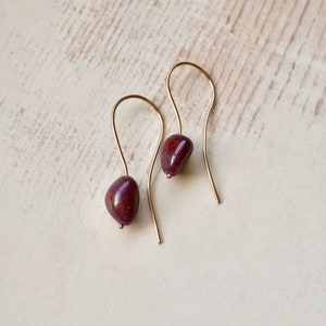 May include: A pair of gold dangle earrings with a deep purple gemstone on each earring.